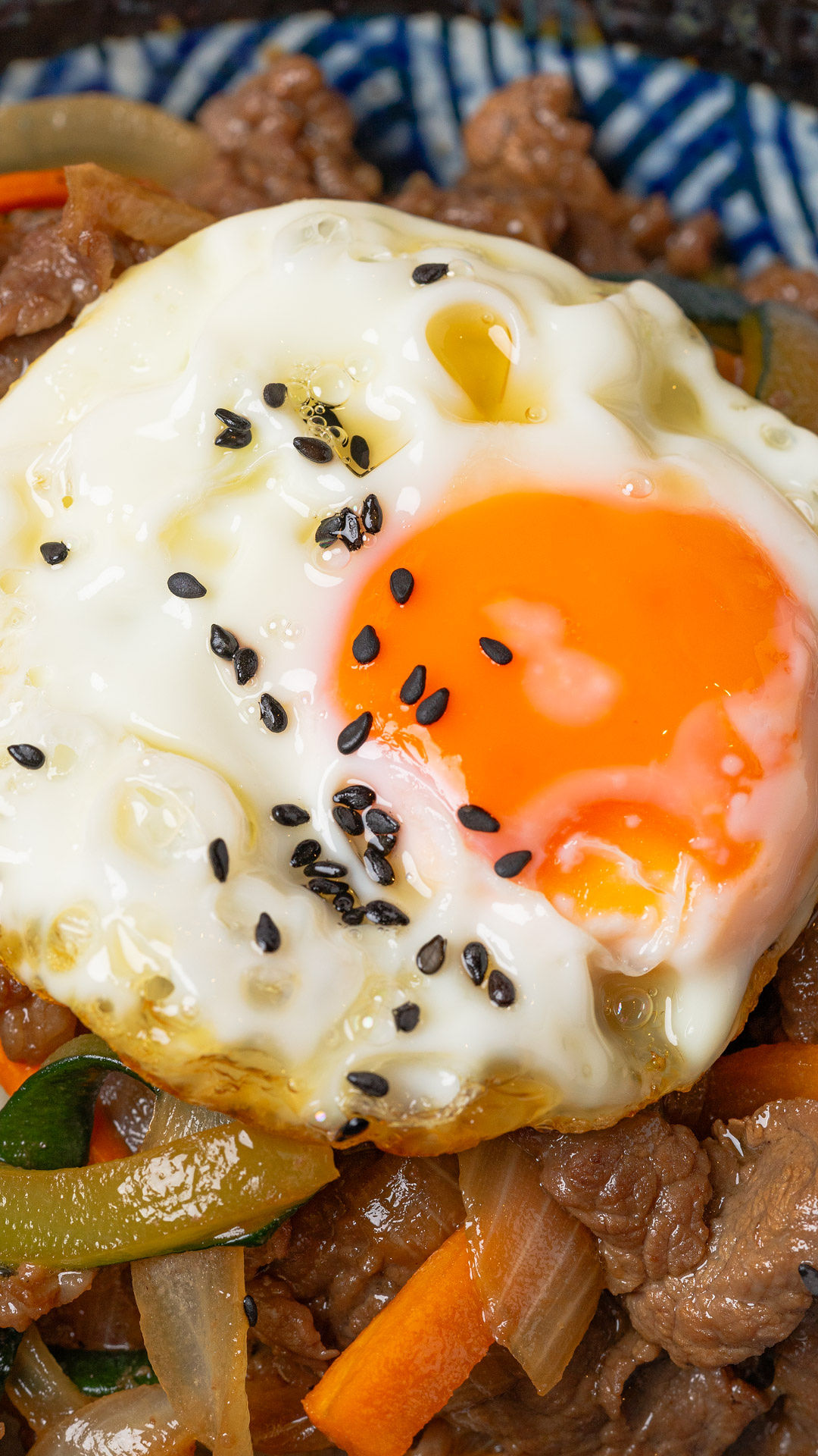 Fried egg over bulgogi with vegetables, in a dosirak bowl