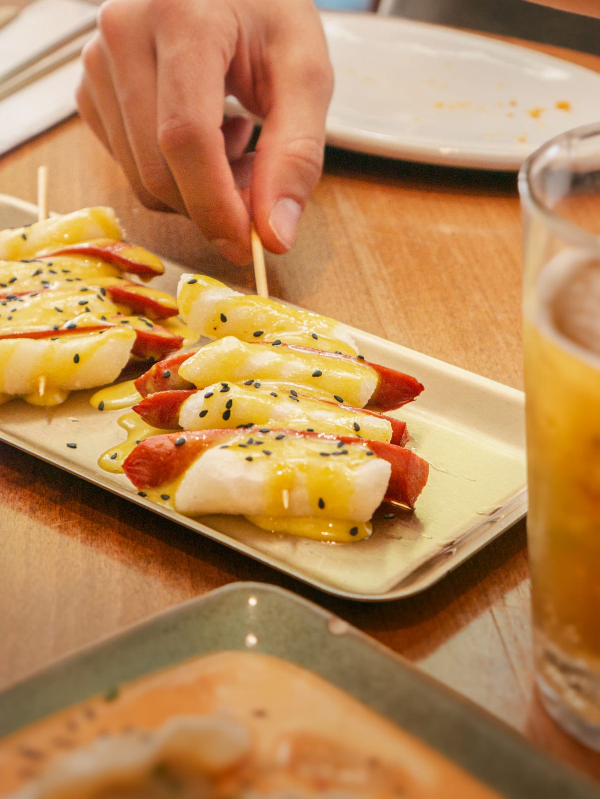 Tteok skewers wrapped in bacon with mustard sauce and sesame
