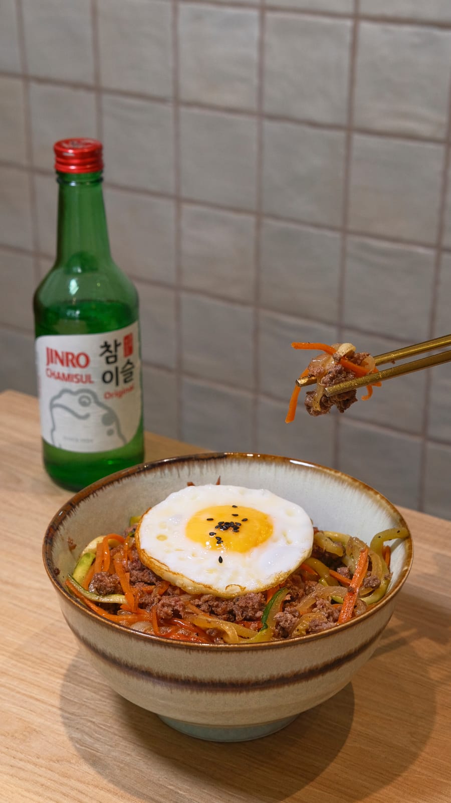 Bulgogi bibimbap with fried egg and vegetables, with a bottle of soju